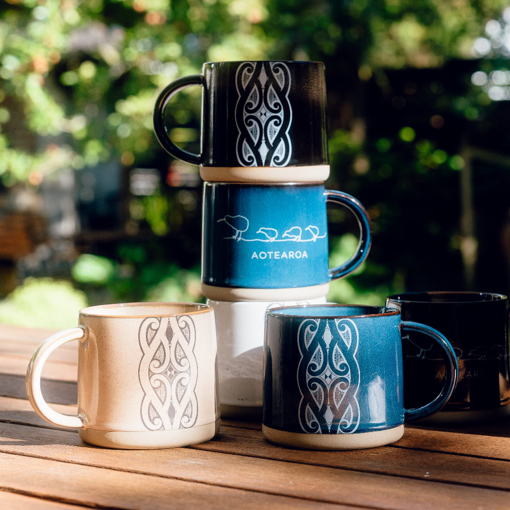 Set ofGlazed Ceramic Mugs with designs and text on a wooden surface outdoors.