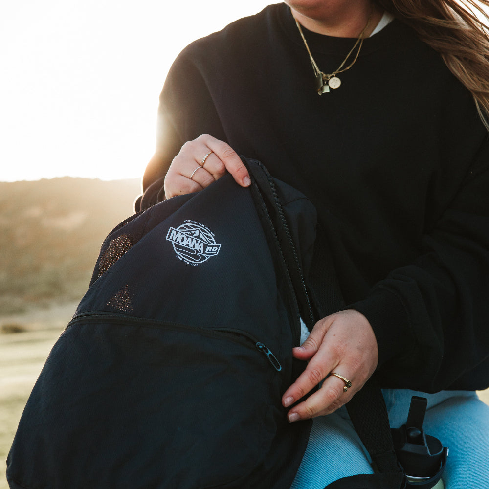 Person holding a packable black backpack with a logo against a natural background