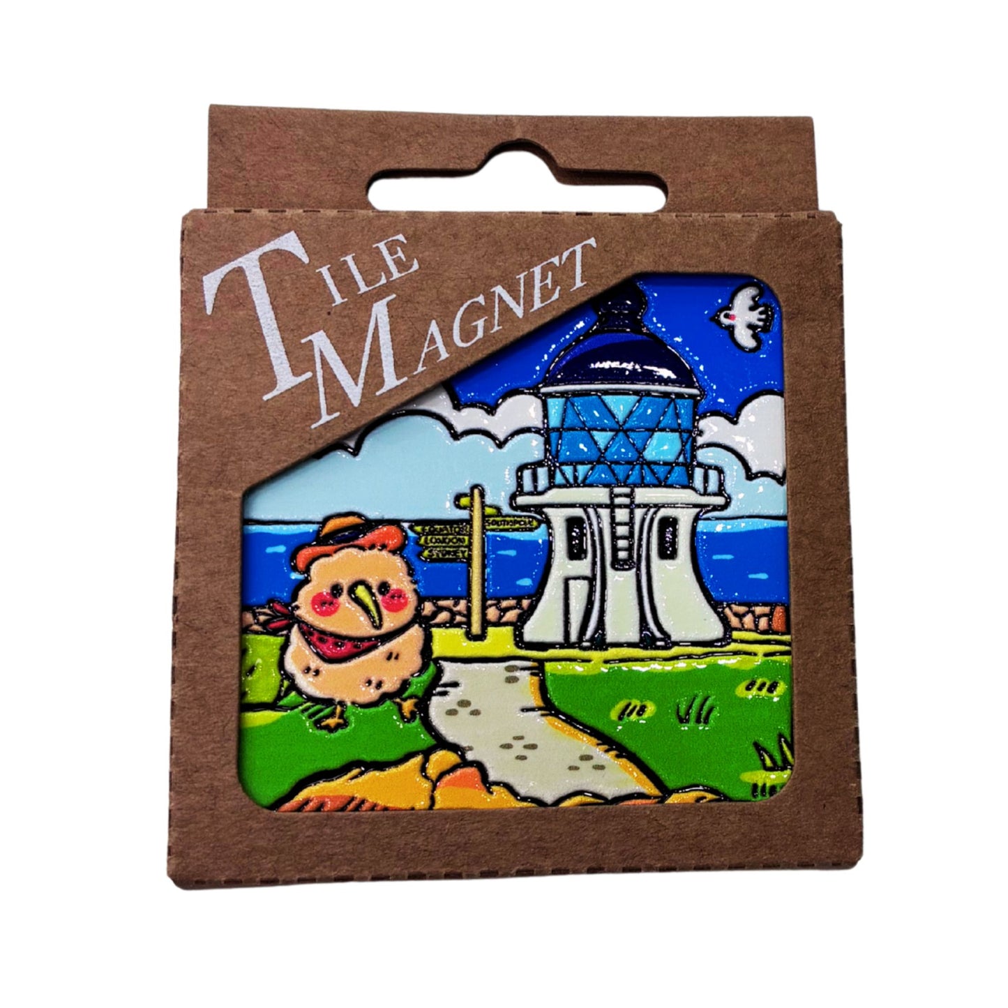 A square ceramic tile magnet in its brown cardboard packaging, featuring a colorful illustration of a lighthouse, a kiwi, and a path under a blue sky.