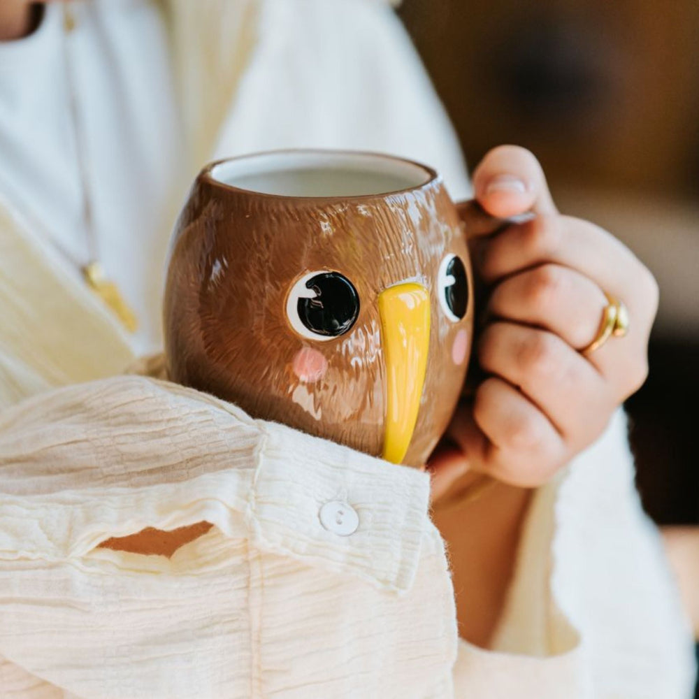 Person holding a brown kiwi-shaped mug with a blurred background