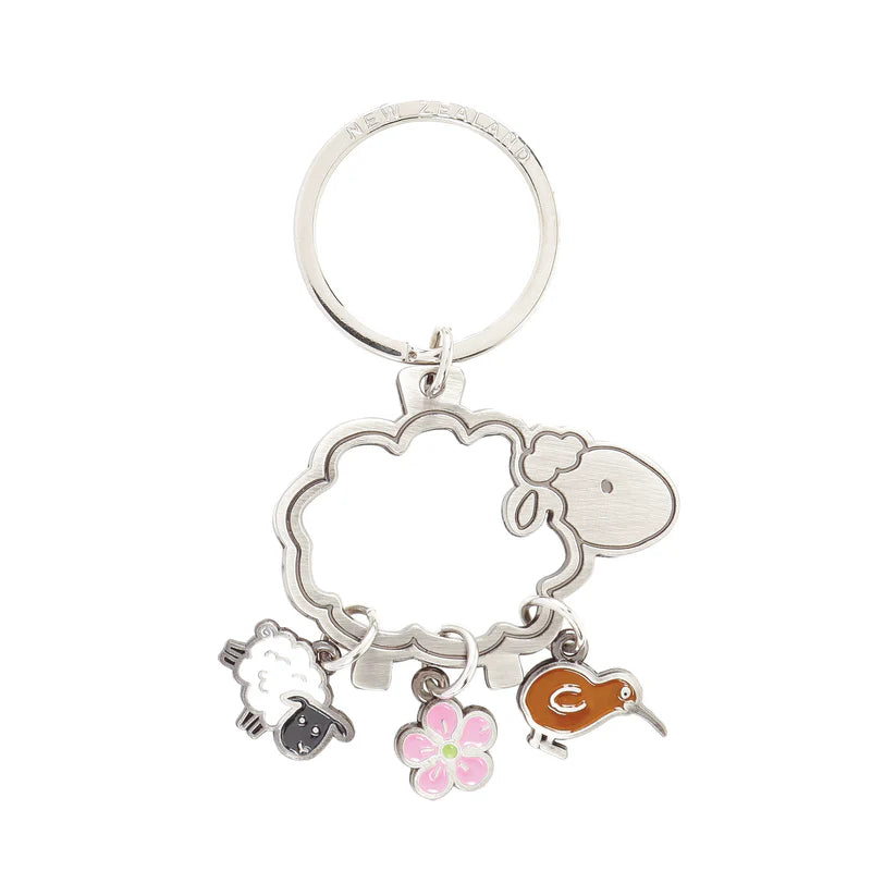 A metallic key ring with a cut-out shape of a sheep, attached charms depicting a sheep, a manuka flower, and a kiwi bird.