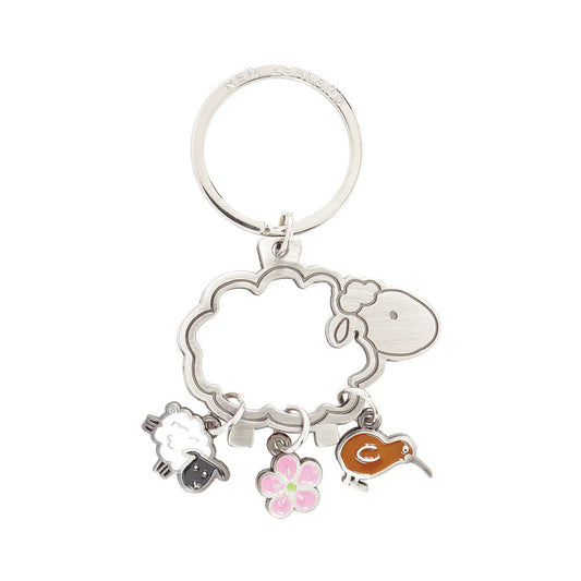 A metallic key ring with a cut-out shape of a sheep, attached charms depicting a sheep, a manuka flower, and a kiwi bird.