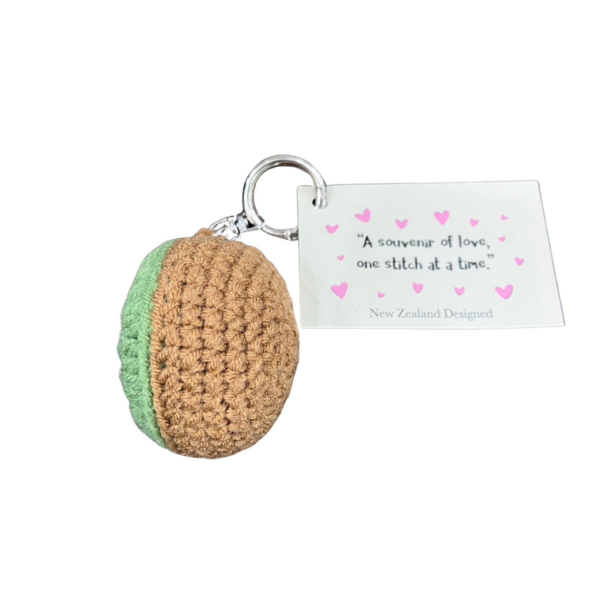 Crocheted keychain with a green and brown kiwifruit design on a white background, featuring a tag with text.
