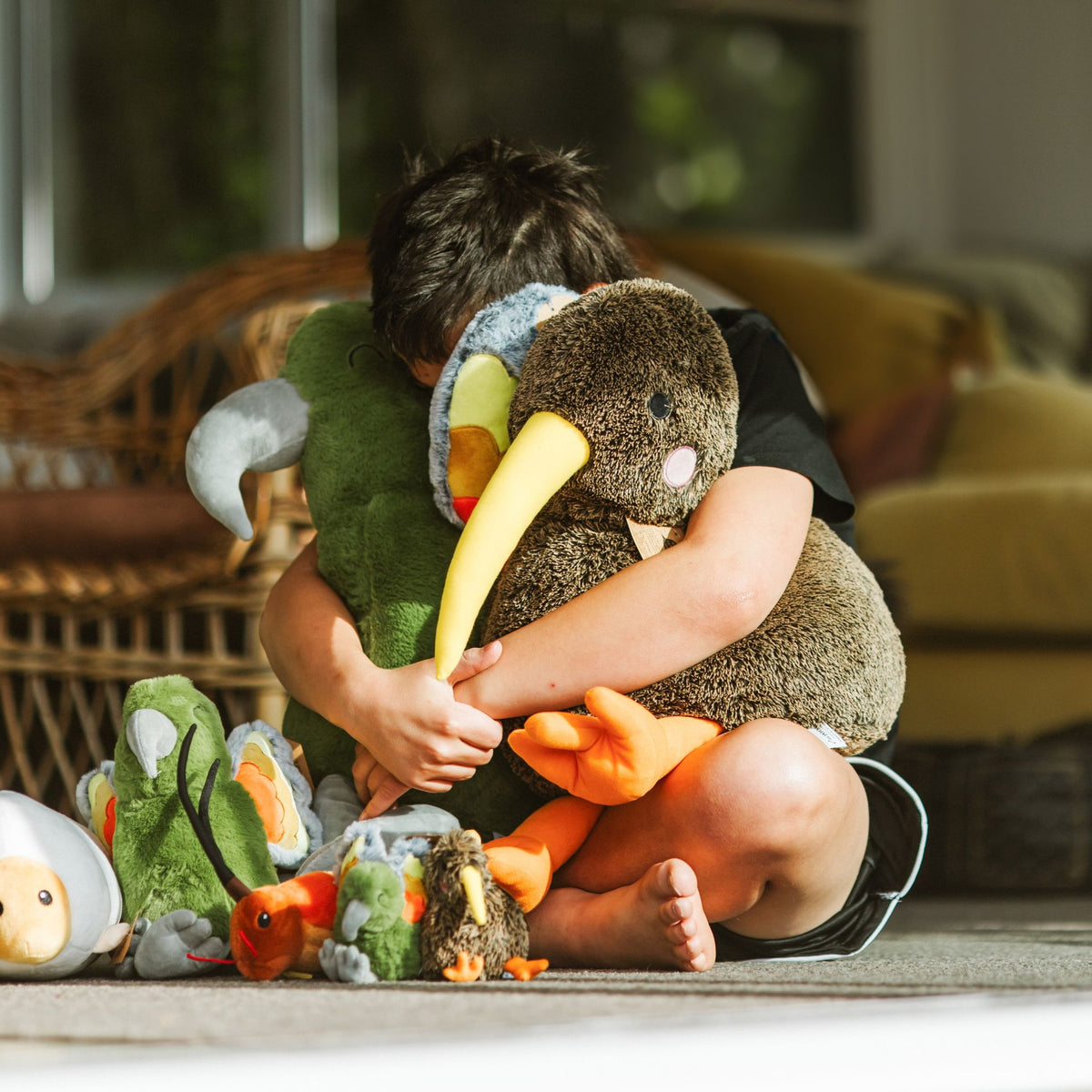 a boy holding kea and kiwi soft toys
