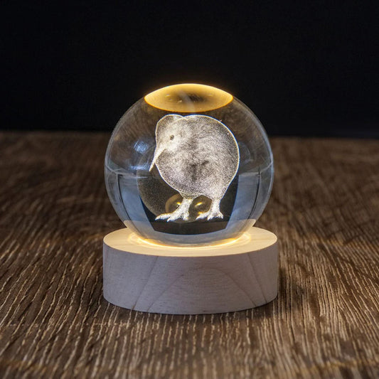 Glass sphere with a kiwi bird engraving on a wooden base, illuminated from below.