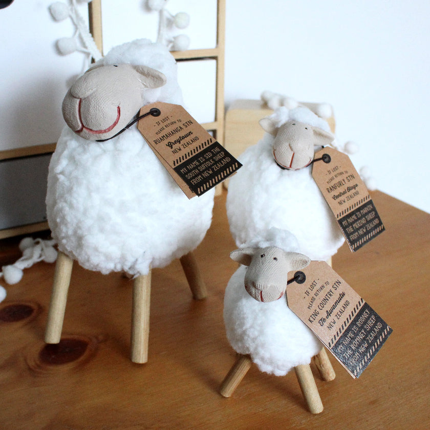 Three sheep figurines with tags on a wooden surface