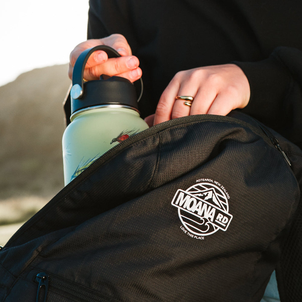 Person holding a green water bottle with a packable black backpack 