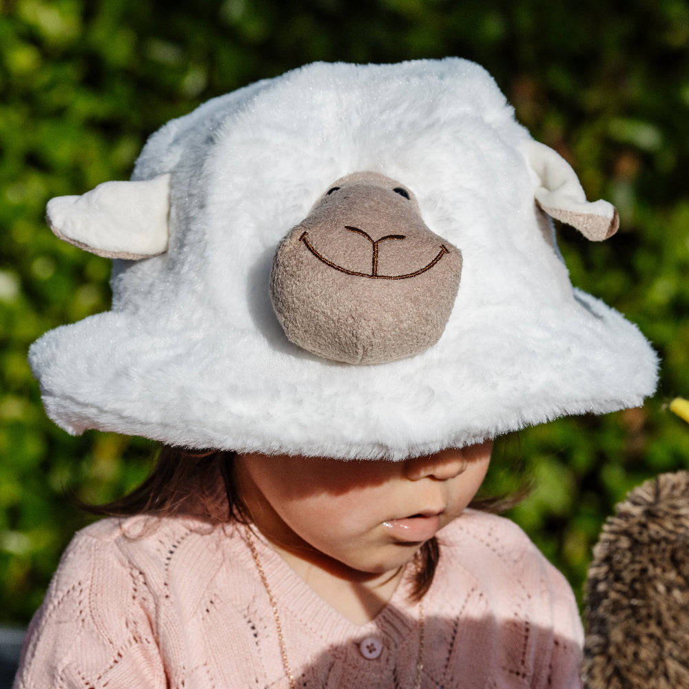Child wearing a fluffy white sheep hat with a green background