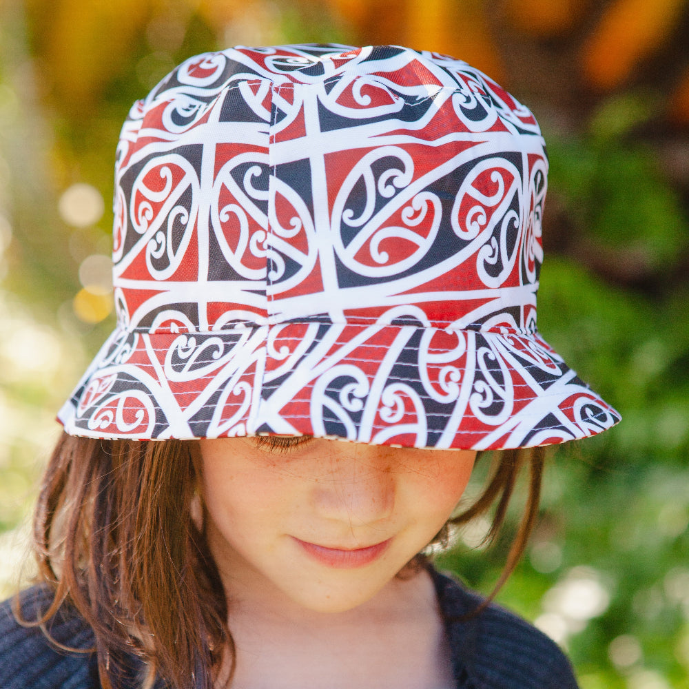 Child wearing a Shop Moana Road Mangopare Bucket Hat patterned bucket hat with a blurred natural background
