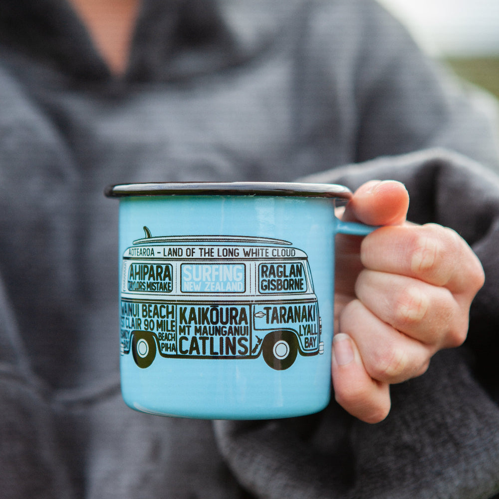 Person holding a blue enamel mug with text and graphics.