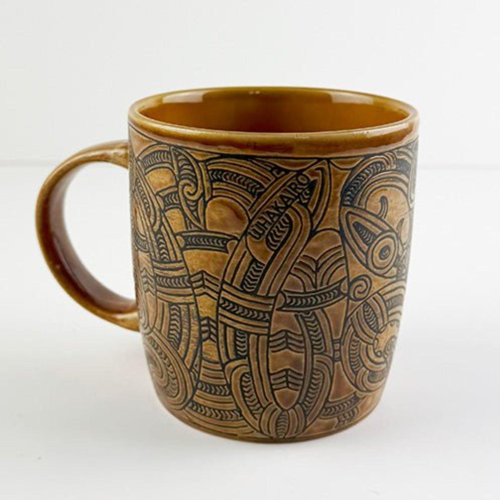 Brown Whakairo ceramic mug with Māori design on a white background
