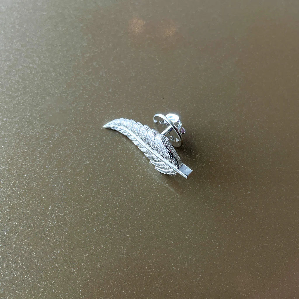 Silver leaf-shaped earring on a textured brown background