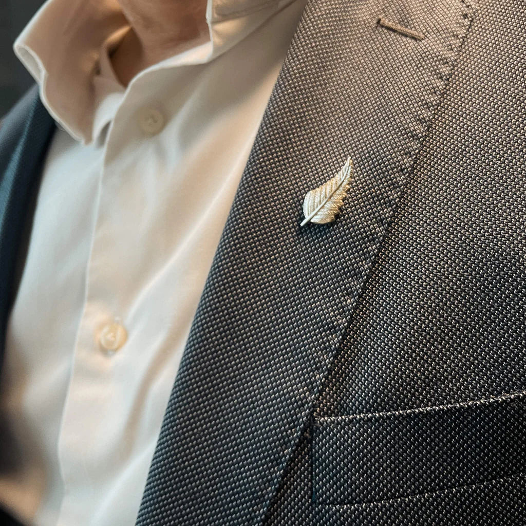 Close-up of a suit jacket with a silver fern pin and a shirt with buttons.
