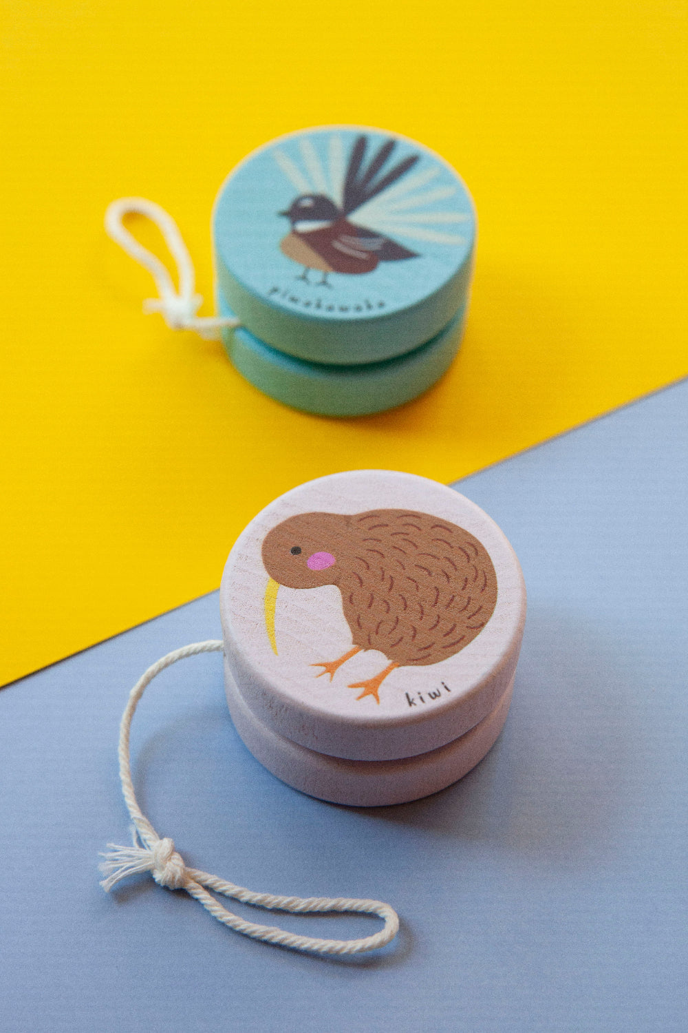 Two wooden yoyos with bird illustrations on a yellow and blue background