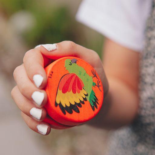 Girl holding a orange yo-yo with a Kea bird design 