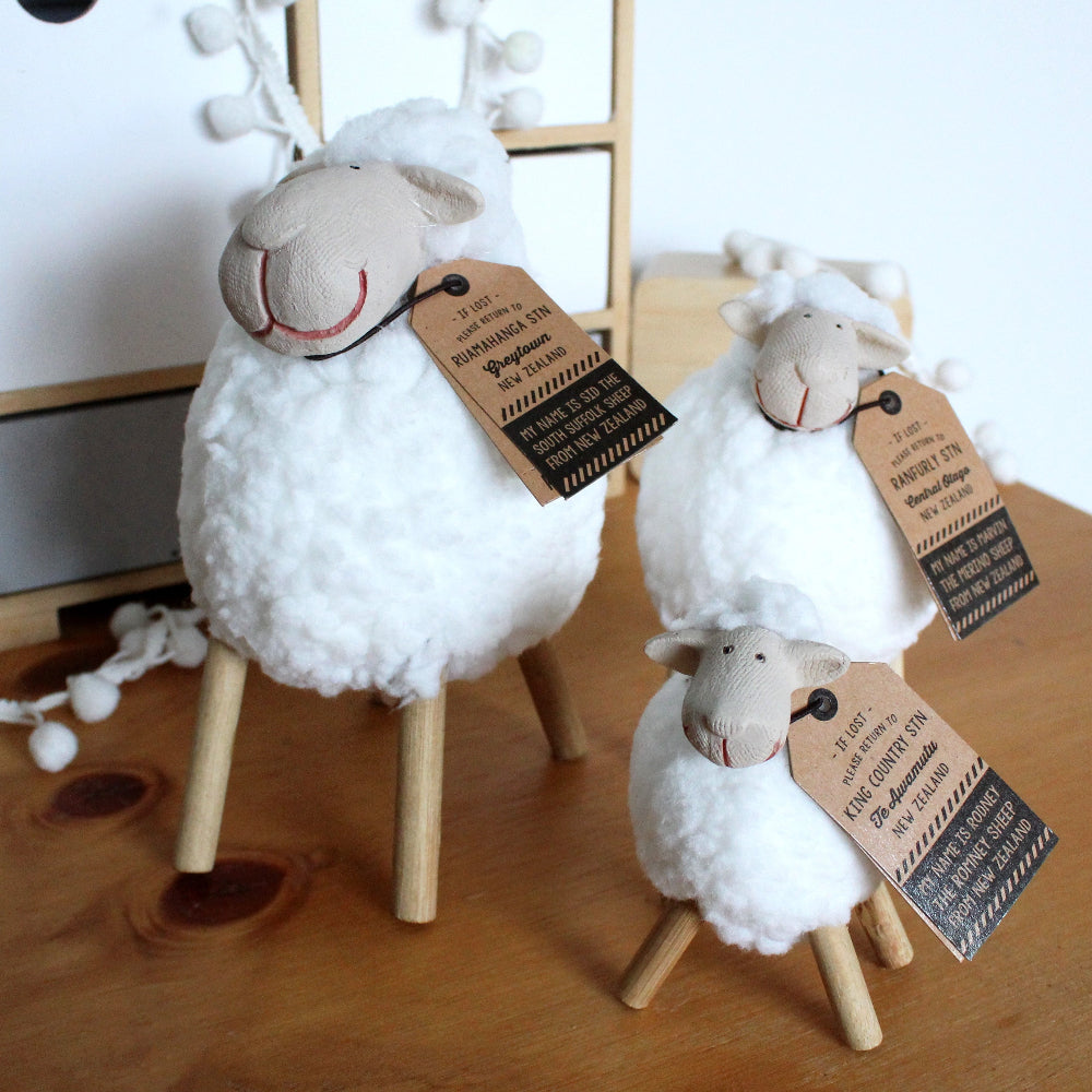 Three woolly sheep figurines with tags on a wooden surface